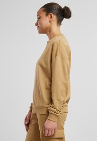 Beige Sweatshirt mit Rundhalsausschnitt, überschnittenen Schultern und gerippten Bündchen. Das Material wirkt weich und leicht strukturiert.