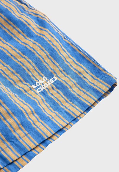 Tissu rayé bleu et beige avec texte brodé blanc « Love Chaos » près de l'ourlet, sur un fond gris clair.