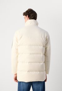 Daunenjacke in Off-White mit gesteppten Abschnitten, hohem Kragen und schwarzem Akzent an den Ärmeln. Glatte Textur mit lockerer Passform.