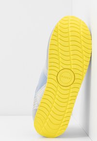 Semelle de basket avec un motif de bande de roulement jaune vif, logo circulaire de la marque au centre portant l'inscription "Scandinavian Woden Sneakers".