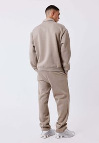 Beige sweatshirt and matching joggers, cotton blend, relaxed fit, ribbed cuffs and waistband, paired with light gray athletic shoes.