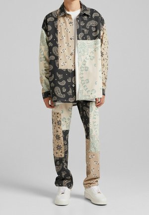 Patchwork Hemd- und Hosen-Set mit verschiedenen Paisley-Mustern in Schwarz, Beige und Türkis, kombiniert mit weißen Sneakern.