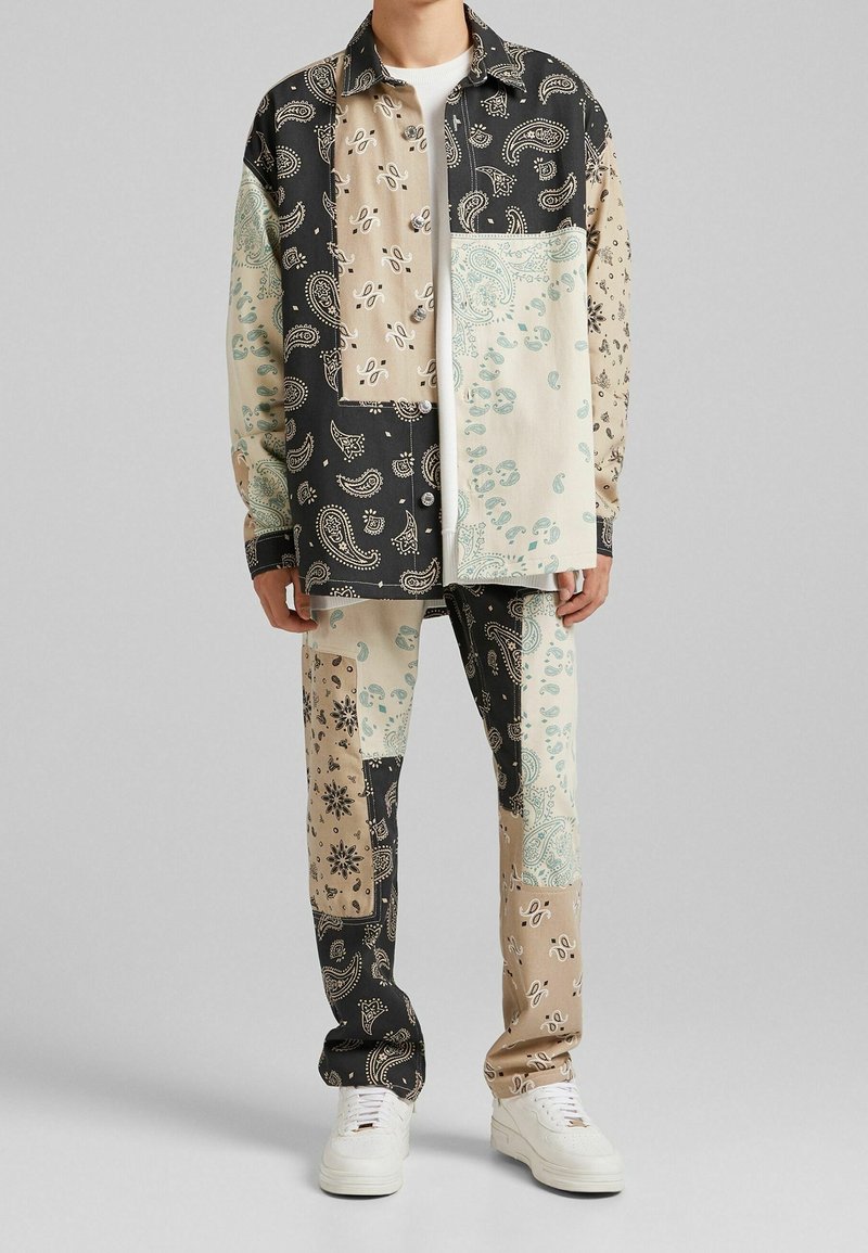Ensemble chemise et pantalon patchwork présentant divers motifs cachemire en noir, beige et nuances de sarcelle, assorti de baskets blanches.
