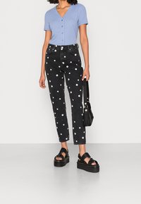 Top azzurro chiaro a coste con maniche corte e scollatura a V, abbinato a jeans neri a vita alta con motivi floreali bianchi e sandali neri chunky.