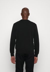 Sudadera negra de manga larga con puños y dobladillo acanalados. Presenta un escote redondeado y una textura suave. Sin logotipos ni patrones visibles.