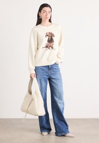 Cremefarvet sweatshirt med grafik af en dachshund, parret med lyseblå brede jeans og en beige skuldertaske.