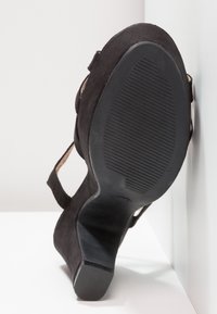 Chaussure à talon haut en daim noir, inclinée vers le haut, montrant une semelle en caoutchouc texturée avec des lignes de grip horizontales et un talon bloc.