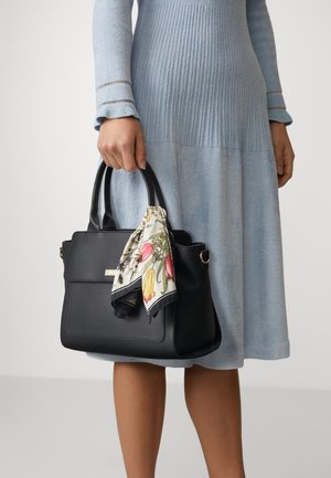 Svart läderhandväska med dubbla handtag, dekorerad med en blommönstrad scarf knuten runt handtaget. Kombinerad med en ljusblå ribbad klänning.