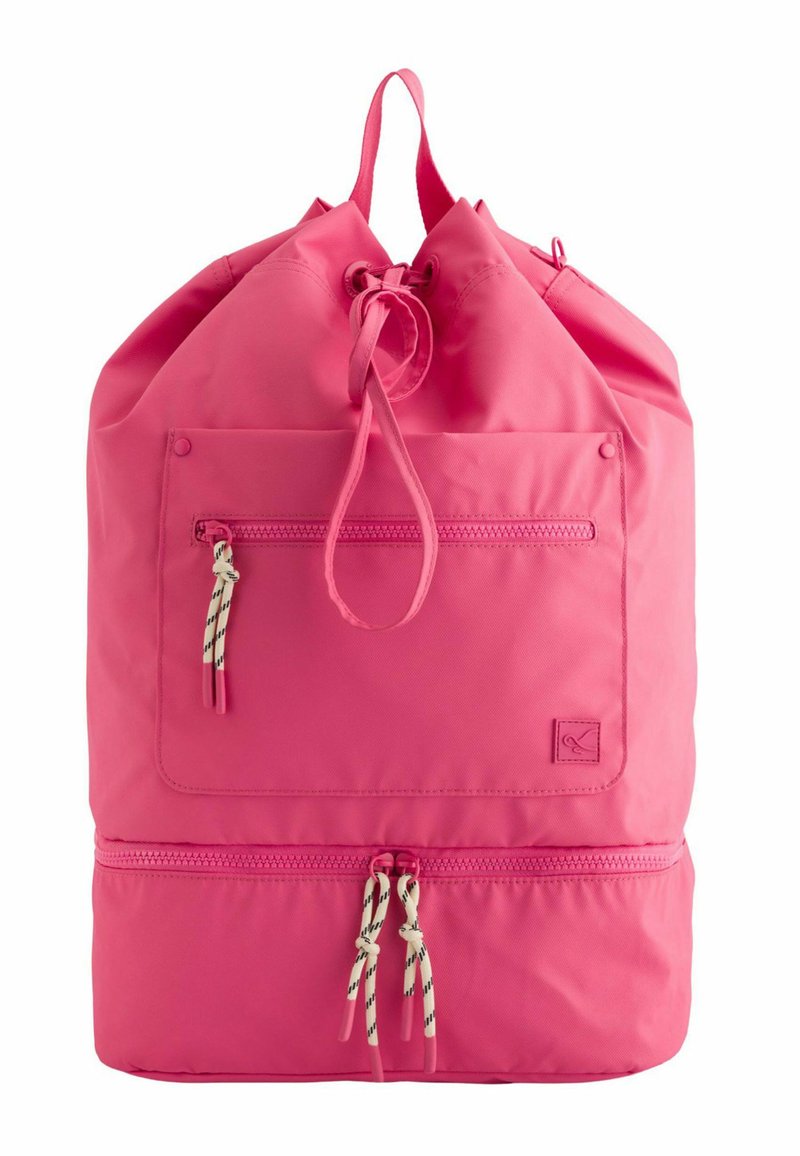 Růžový batoh na stažení vyrobený z odolné tkaniny, s přední kapsou na zip a kontrastními černobílými šňůrkami.