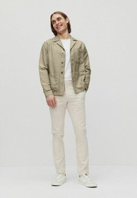 Linned button-up jacka i ljusbeige, med två framfickor, kombinerad med krämfärgade slim-fit byxor och vita sneakers.