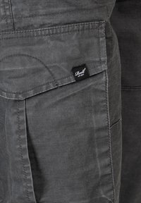 Graue Baumwoll-Cargo-Hosen mit sichtbaren Nähten, mehreren Taschen und einem schwarzen Markenlabel an der Seite. Weicher, strukturierter Stoff.