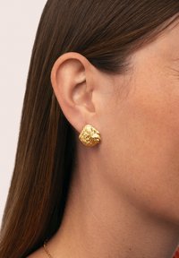 Orecchino a perno in oro con un design scultoreo, caratterizzato da una superficie leggermente sollevata e irregolare che aggiunge interesse visivo.