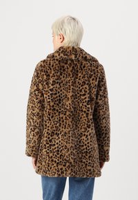 Leopardprint nepbontjas, bruine basis met zwarte vlekken, lange mouwen, kraag en een relaxte pasvorm. Model draagt blauwe jeans.