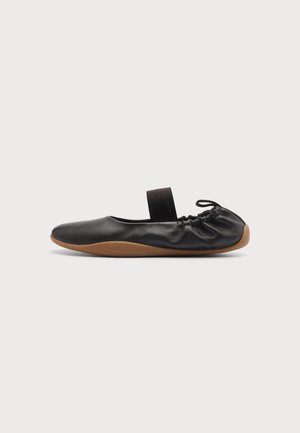 Ballerine en cuir noir avec bride élastique et semelle souple marron, vue de profil sur un fond uni.