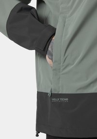 Voděodolná bunda v světle zelené a černé barvě, s nastavitelnými manžetami, kapsou na zip a logem Helly Tech® na lemu. Texturovaná tkanina.