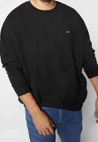 Sweatshirt noir à manches longues avec poignets côtelés, encolure ronde et petit logo rouge Levi's sur la poitrine, en coton doux.