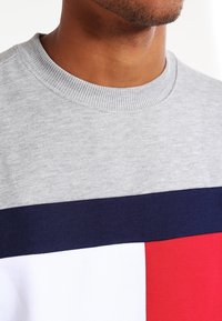 Felpa grigia con collo rotondo caratterizzata da blocchi orizzontali blu navy, bianchi e rossi. Il tessuto sembra morbido e con una finitura testurizzata.