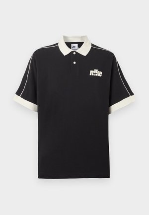 Polo nera a maniche corte con colletto e polsini bianchi, piping bianco sulle maniche e logo Nike bianco sul petto a sinistra.