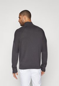 Dunkelgrauer Strickpullover mit hohem Kragen, gerippten Akzenten an den Schultern und taillierten Bündchen. Weiche Textur und lässige Silhouette.