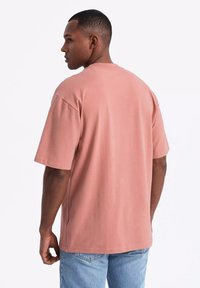 Tričko s krátkým rukávem a kulatým výstřihem z prachově růžové bavlny. Uvolněný střih se hladkým povrchem, v kombinaci s vybledlými modrými džínami.