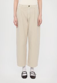 Beige wide-leg trousers with front pleats, button closure, side pockets, and a smooth cotton texture. Paired with black shoes and white socks.
