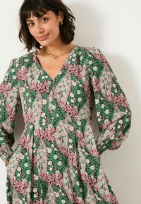 Blumendruckkleid in Grün, Pink und Flieder mit V-Ausschnitt, langen Puffärmeln und Taschen. Mit aufwendigen Blatt- und Blütenmustern.