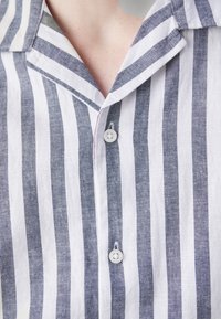 Gros plan d'une chemise à rayures verticales blanches et grises avec deux boutons fermés et un col visible au niveau de l'encolure.
