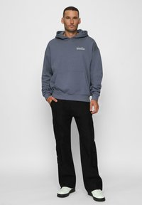 Felpa con cappuccio grigio ardesia con tasca frontale e dettaglio del logo, abbinata a pantaloni cargo neri con tasche laterali e gambe affusolate.