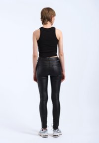 Czarny krótki top na ramiączkach, dopasowane czarne skórzane spodnie z tylnymi kieszeniami oraz białe sneakersy z niebieskimi akcentami. Gładka faktura, elegancki design.