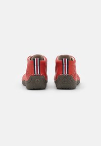 Bottes de cheville en cuir rouge avec une texture lisse, ornées d'un accent en tissu rayé à l'arrière et d'une semelle en caoutchouc gris robuste.