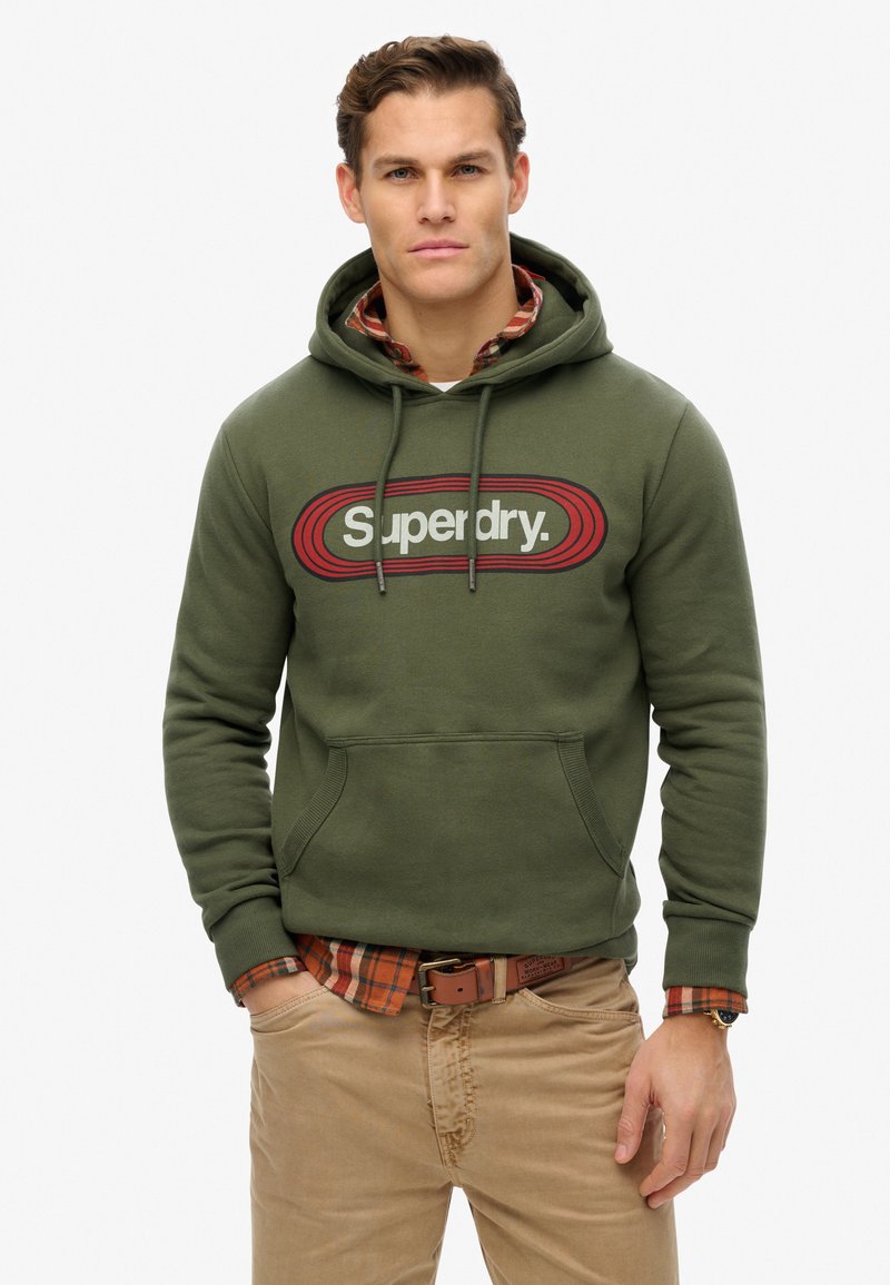 Zielona oliwkowa bluza z kapturem z grafiką z przodu, na której widnieje napis "Superdry". Posiada kieszeń kangurkę, kaptur ze sznurkiem oraz ściągacze przy rękawach.