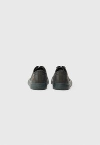 Black low-top sneakers with a textured finish, featuring a reinforced heel, rubber sole, and subtle logo detail on the side.