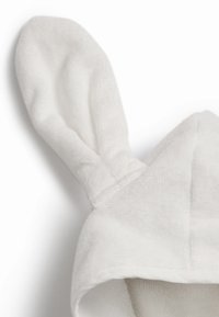 Vit handdukshuvtröja med två kaninöron på toppen. Mjuk, texturerad tyg med en enkel design. Kanterna är snyggt sydda.