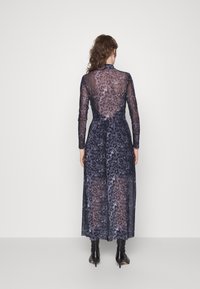 Langes, durchscheinendes Kleid in dunklen Farben mit floralen Mustern, langen Ärmeln und tailliertem Schnitt, kombiniert mit knielangen schwarzen Stiefeln.