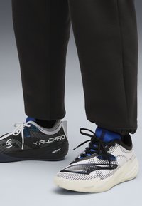 Des chaussures de sport dotées d'un design à rayures noires et blanches, de matériaux texturés, de semelles flexibles et de lacets contrastants. Deux styles distincts visibles.