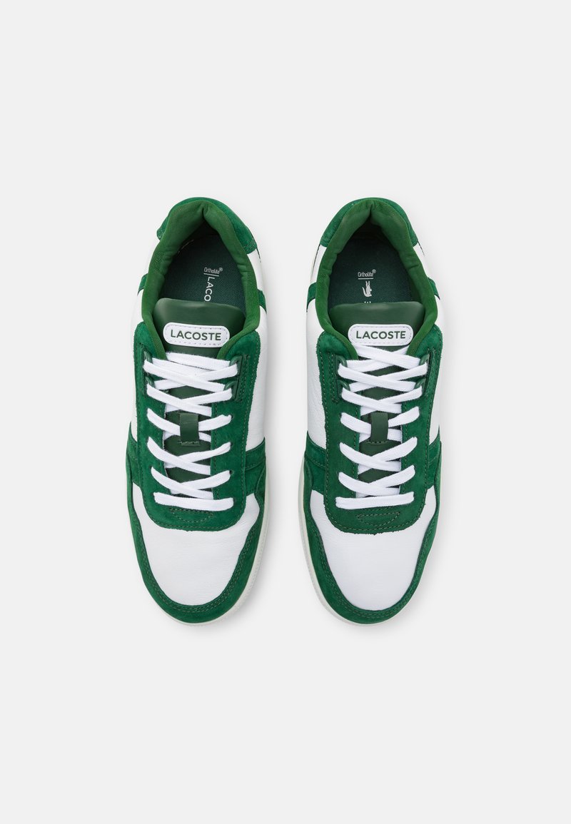 Witte en groene sneakers van suede en leer, met een vetersluiting, ronde neus en het 'LACOSTE' logo op de tong.