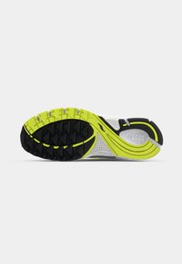 Semelle de chaussure de sport avec motifs d’adhérence noirs et jaune fluo, semelle intermédiaire blanche texturée et motif de bande de roulement incurvé sur fond blanc.