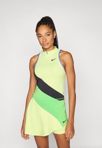 Αμάνικο φόρεμα Nike σε ανοιχτό πράσινο χρώμα με μαύρες και σκούρες πράσινες λεπτομέρειες, με φερμουάρ μπροστά και αθλητικό σχέδιο.