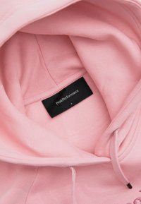 Rosa Sweatshirt mit weicher Textur, ausgestattet mit Kapuze, Kordelzug und einem schwarzen Etikett, das den Markennamen "PeakPerformance" und die Größe "S" zeigt.
