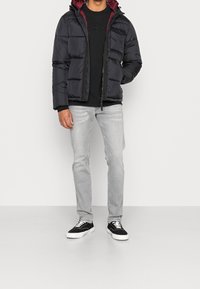 Prošívaná bunda v černé barvě s vínovou podšívkou, nošená přes černé tričko. Kombinováno se světle šedými džíny a černými teniskami s bílými podrážkami.