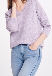 Un pull tricoté violet clair avec un col en V, des poignets côtelés et une coupe décontractée, associé à un jean taille haute bleu clair.