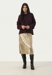 Maglione a maglia bordeaux con polsini a coste, abbinato a una gonna di paillettes oro al ginocchio e stivali neri alti fino al ginocchio. Design semplice e finiture con texture.