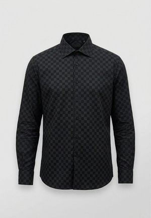 Chemise noire à manches longues et boutonnée, avec un discret motif à carreaux foncés et un col pointu, sur fond clair.