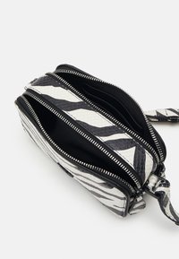 Bolso con estampado de cebra en blanco y negro, con múltiples compartimentos con cremallera, fabricado en material texturizado, que cuenta con cremalleras en tono plateado y una correa para la muñeca.