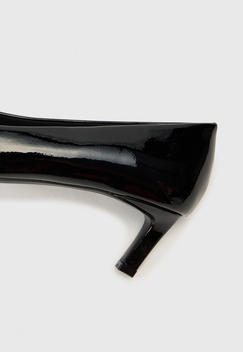 Zapato de tacón alto de charol negro con punta afilada y tacón bloque de altura media. Textura lisa y brillante con un diseño sin costuras.