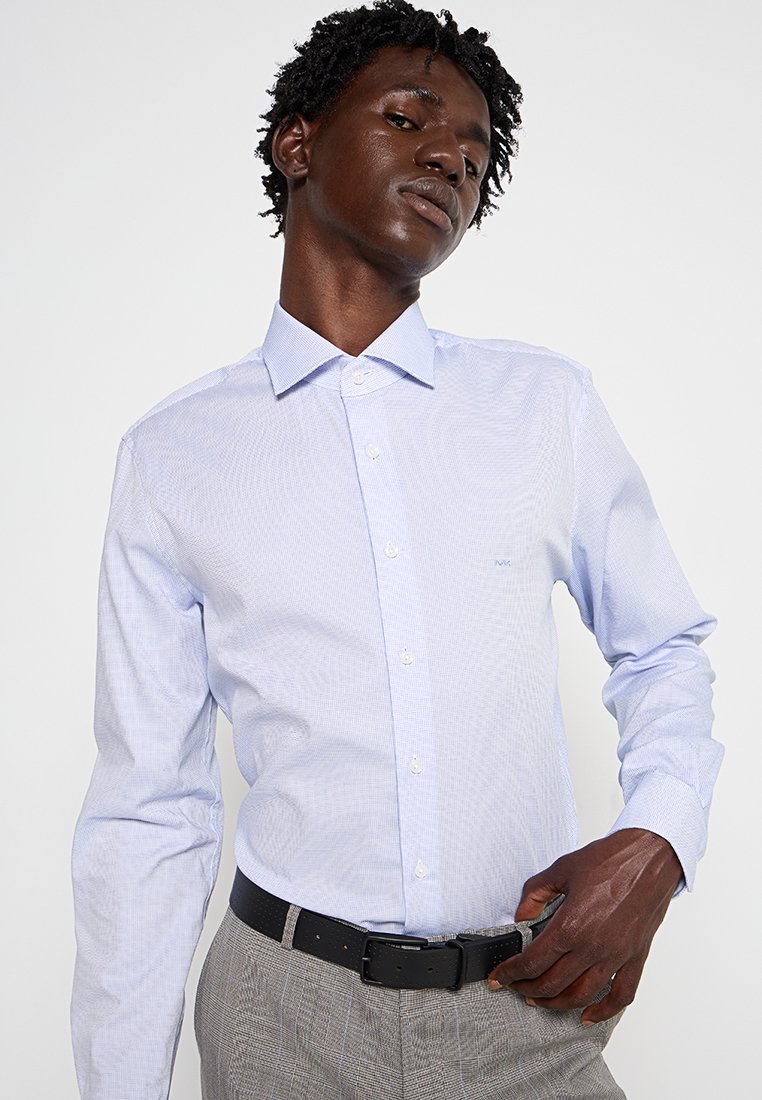 Camisa de vestir de cuadros en azul claro con cuello de punta, mangas largas y frente abotonado. Se lleva con un cinturón negro y pantalones grises con estampado.