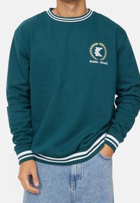 Felpa color teal con colletto e polsini a righe bianche. Presenta un piccolo logo ricamato e un design a girocollo.