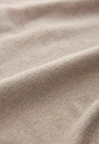 Beiger Baumwollstoff mit glatter Textur, der ein dezentes Strickmuster und leichte Falten zeigt, was seine Weichheit und Flexibilität betont.