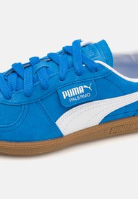 Blauwe suede sneakers met witte accenten en een gestructureerde bruine rubberen zool. Voorzien van een merklabel en blauwe vetersluiting.