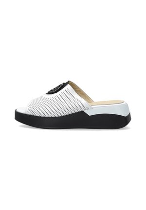 Witte geperforeerde slip-on sandaal met zwarte plateauzool en open teen, met een decoratief cirkelvormig embleem bovenop.